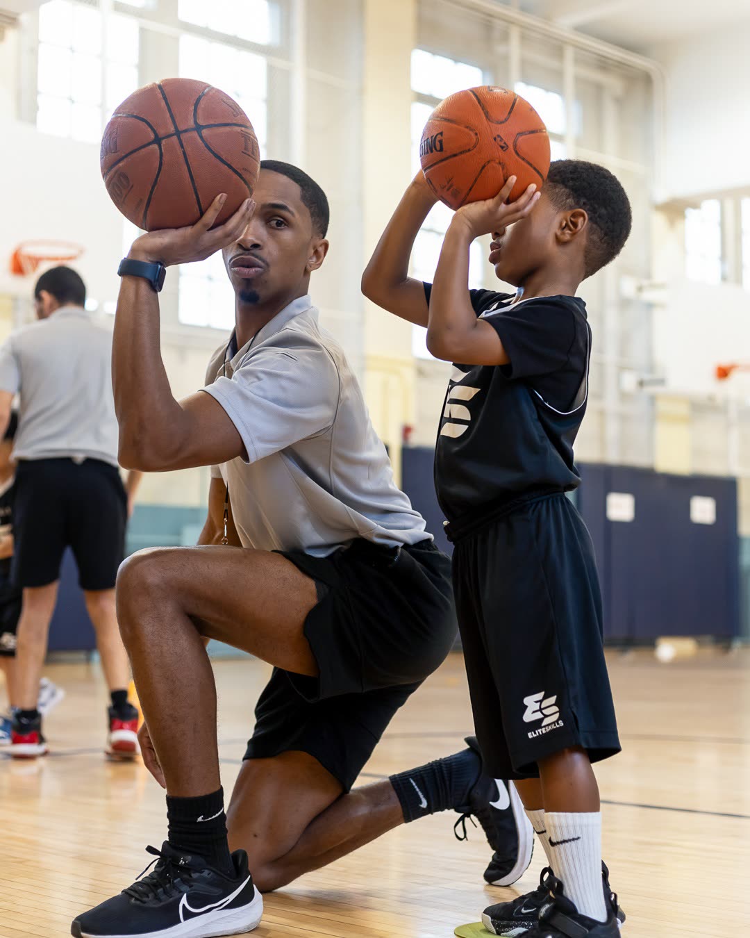 Elite Skills coach kneeling to demonstrate shooting form with a young player